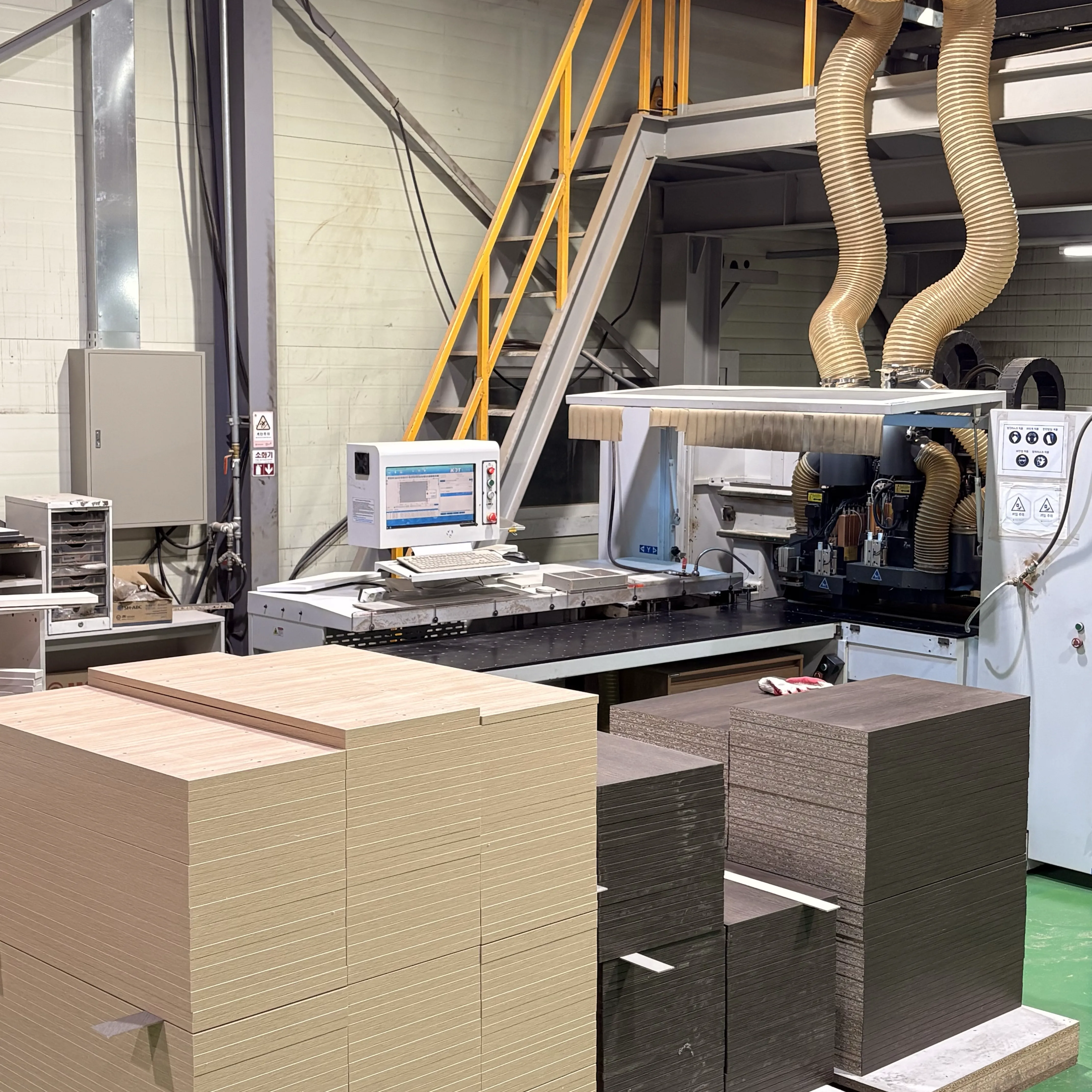CNC 머신과 컴퓨터 모니터, 적재된 목재 패널
